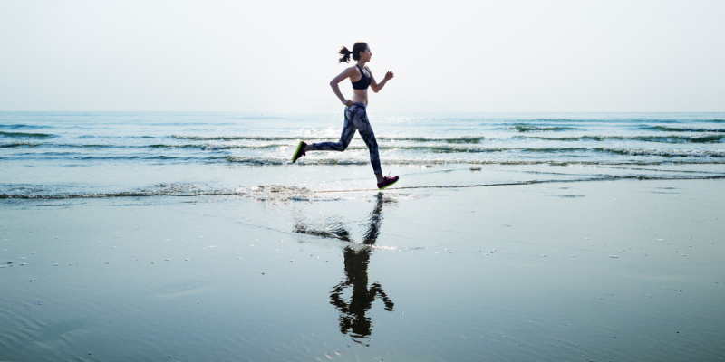 donna fisico atletico corre sulla battiglia mare acqua azzurra tenuta fitness top nero