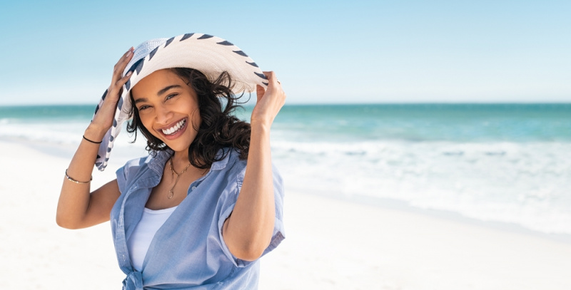 bella donna si tiene cappello paglia bianca spiaggia mare estate sorriso