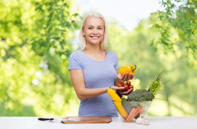 donna sorriso capelli biondi tagliere legno coltello ciotola vetro verdure peperone e pomodori mani