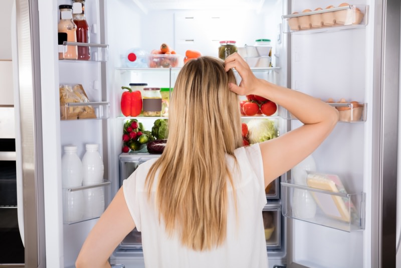 donna capelli biondi di spalle guarda interno frigorifero cibo