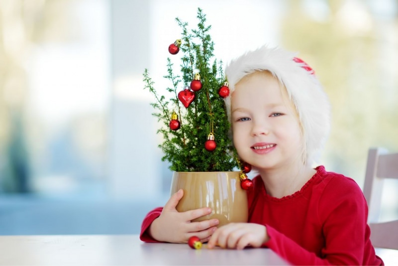 adorabile bellissima bambina vestita di rosso sorride e abbraccia piccolo albero di Natale decorato