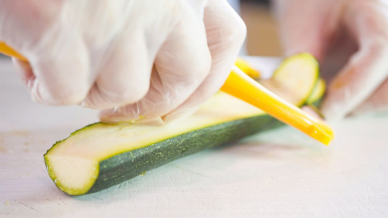 mano con guanto taglia fetta sottile zucchina con pelapatate