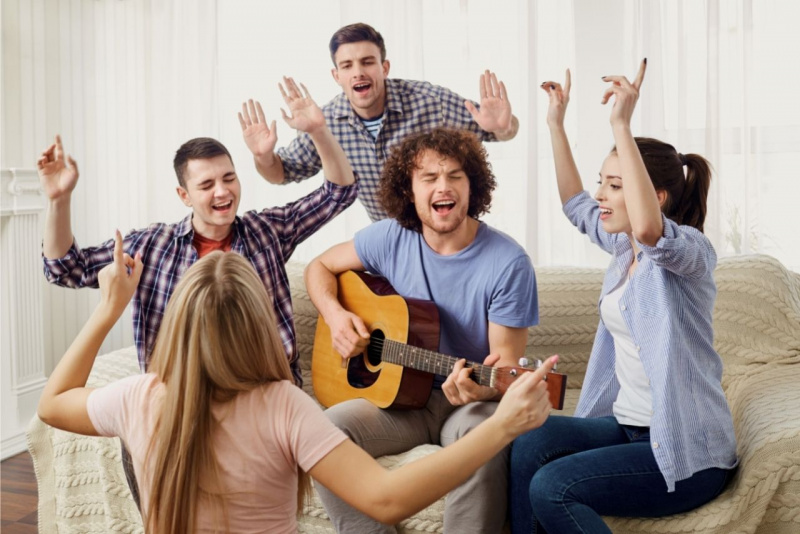 amici che si divertono e cantano seduti divano di casa uomo suona chitarra