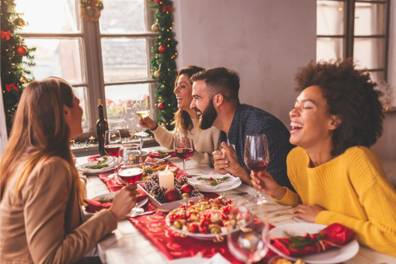 antipasti natalizi runner rosso tavola albero di natale donne uomoni sorridono brindisi calice vino rosso finestra