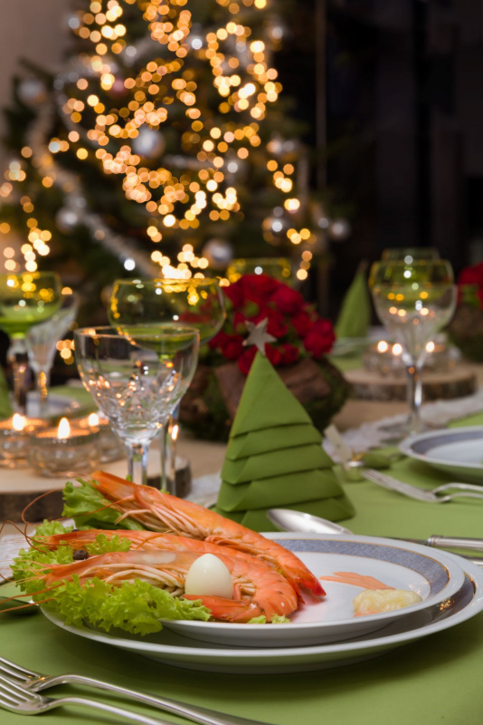 Antipasto di Natale con gamberoni su piatto decorato, tovagliolo verde piegato a forma di albero di Natale e centrotavola festivo con candele.