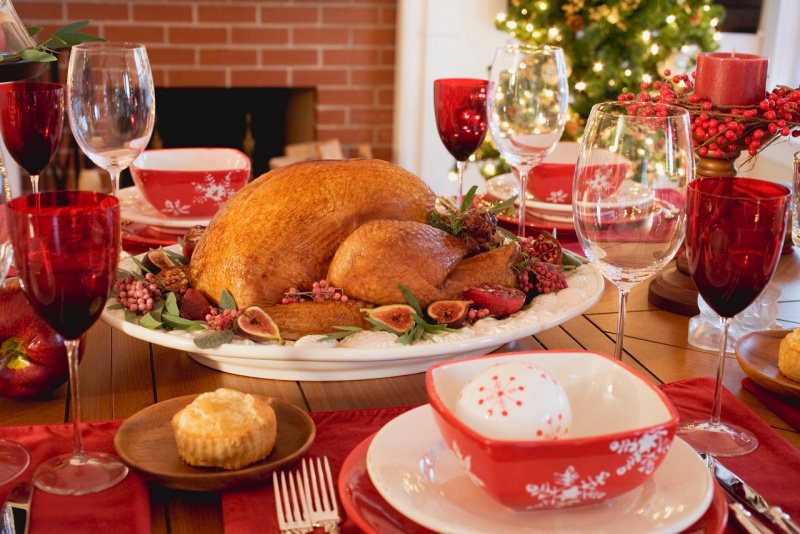 tavola apparecchiata in rosso a festa arrosto di tacchino calici luci albero di natale