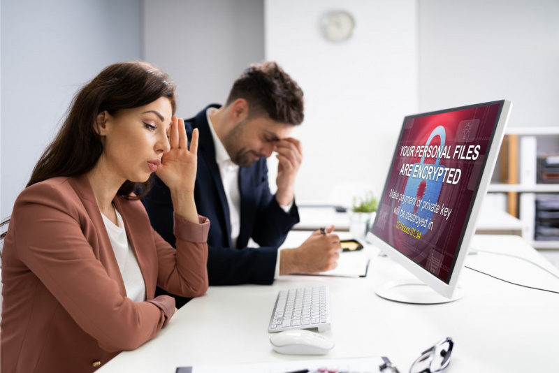 donna e uomo in ufficio afflitti per attacco hacker informatico monitor computer ufficio