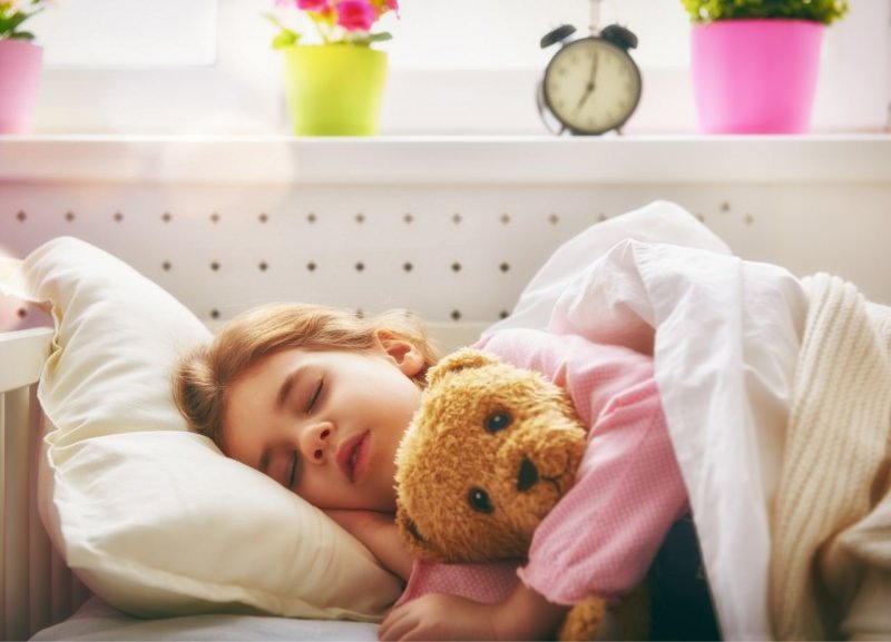 bambina dorme nel letto con il suo peluche orsetto