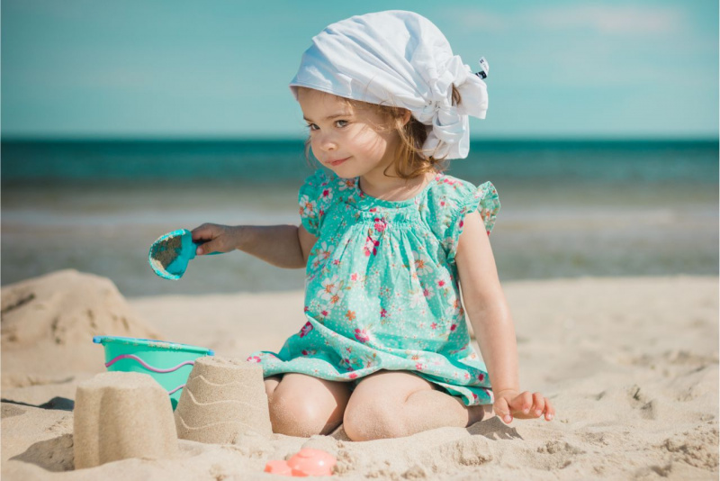 bella bambina abito leggero turchese fantasia a fiori tiene paletta in mano mentre gioca sulla spiaggia al mare con la sabbia