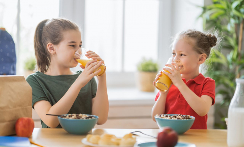 sane abitudini colazione casa bambini bere succo arancia mela rossa ciotole cereali