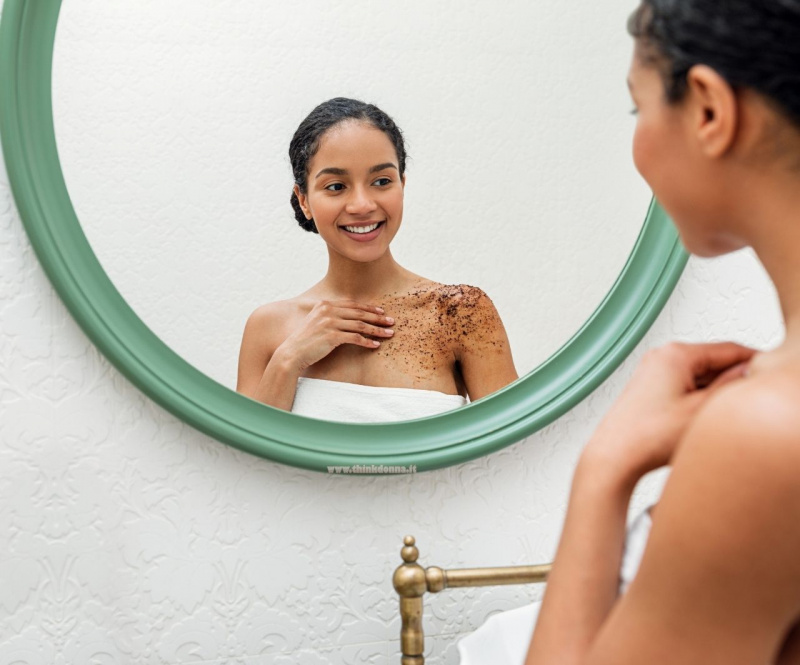 bella donna applica scrub al caff sulla pelle mentre si guarda allo specchio sorriso