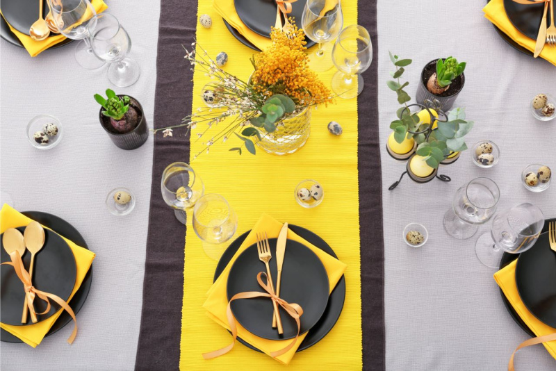 tovaglia grigia con due runner uno grigio scuro euno giallo piatti neri posate oto vasi giacinti calici vetro vaso mimose 