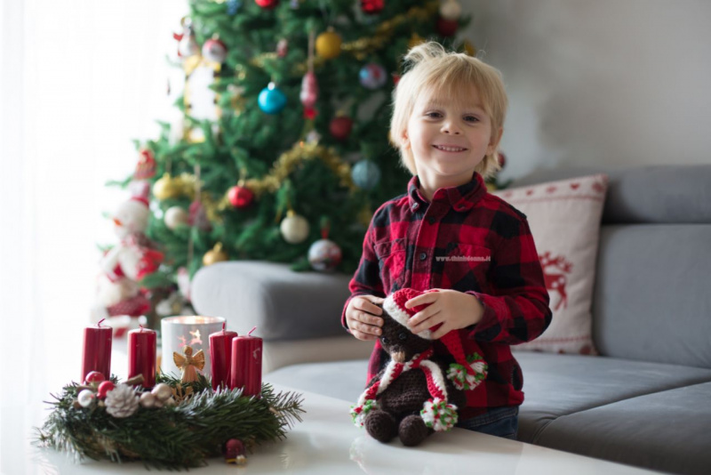 bellissimo bambino felice sorride in soggiorno davanti Albero di Natale e Corona Avvento candele