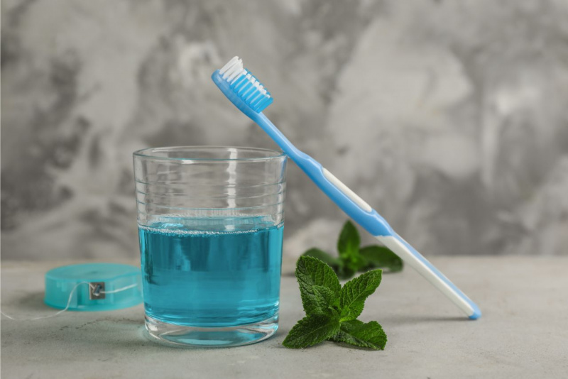 spazzolino da denti poggiato su bicchiere con collutorio blu filo interdentale