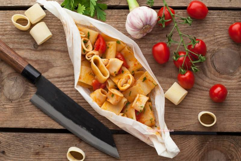 calamarata al cartoccio primo piatto pronto ingredienti aglio pomodorini prezzemolo pasta tagliere legno