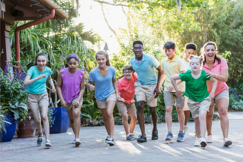 bambini e ragazzi corrono con donna adulta divertimento inclusione sindrome down vita sociale sorrisi