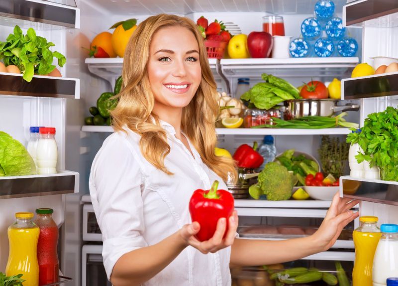 bella donna bionda prende peperone rosso dal frigo pieno di spesa frutta verdure acqua succhi