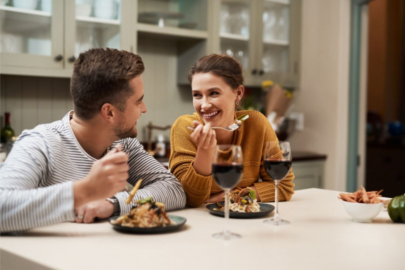 uomo e donna si guardano sorridendo mentre mangiano cena romantica cucina