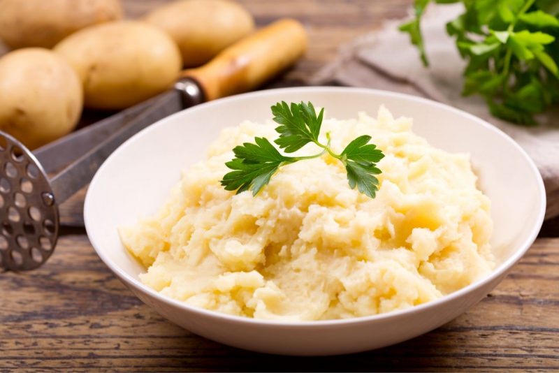 Ciotola con pur di patate foglie di prezzemolo schiacciapatate tavolo legno