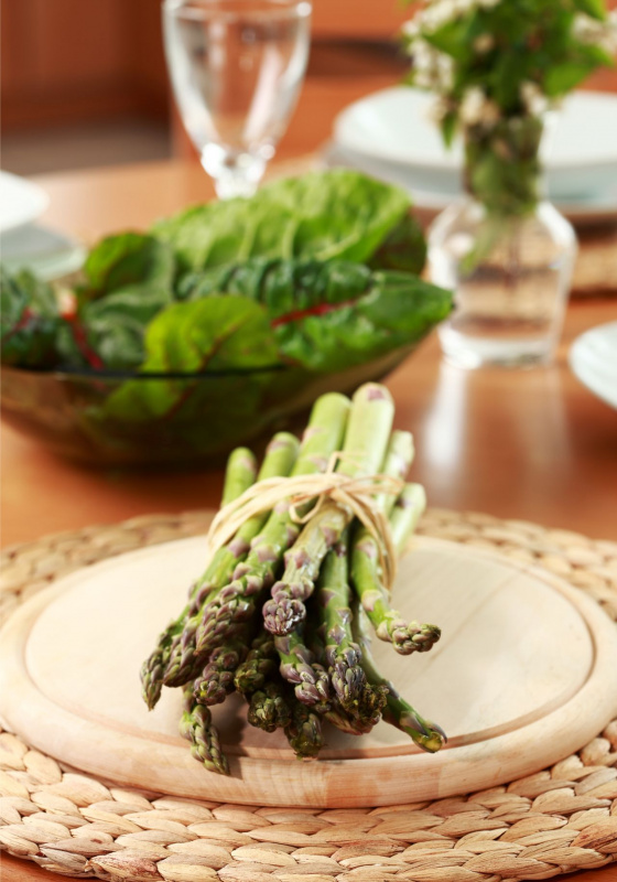 primo piano mazzetto asparagi su piatto legno sullo sfondo foglie di spinaci