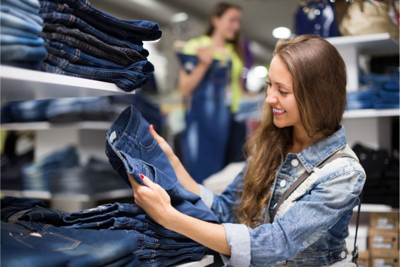 giovane donna capelli castano chiaro sorridente guarda paio jeans negozio