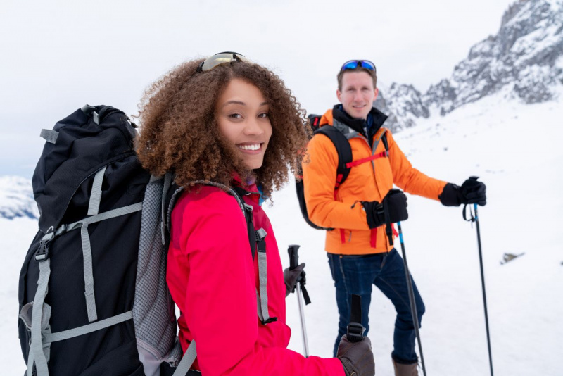 bella donna sorriso denti bianchi capelli ricci afro zaino abbigliamento tecnico uomo bastoni trekking