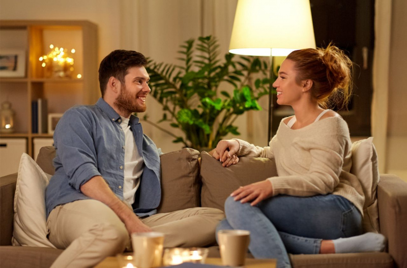 complicità di coppia uomo donna si guardano sorridenti soggiorno seduti sul divano