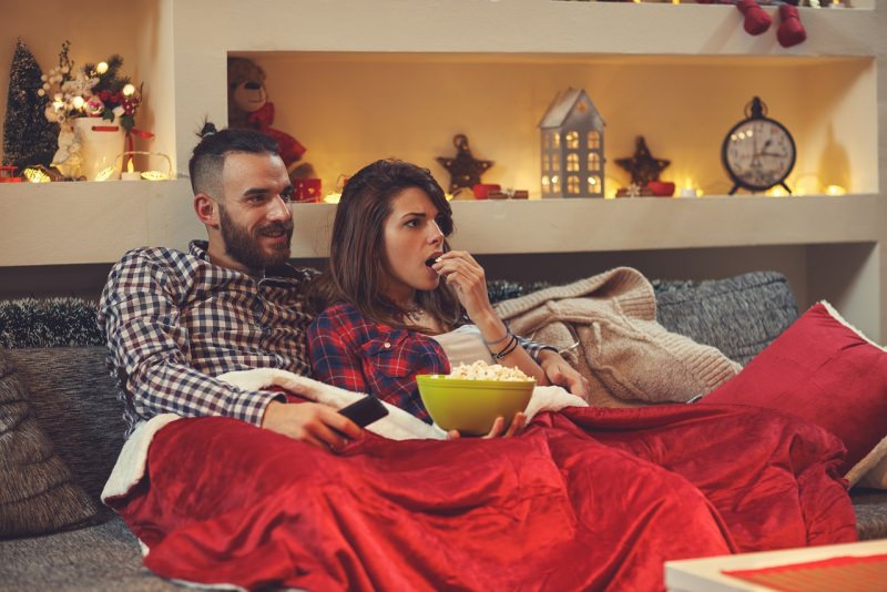 coppia uomo donna maniano popcorn mentre guardano TV divano soggiorno luci 