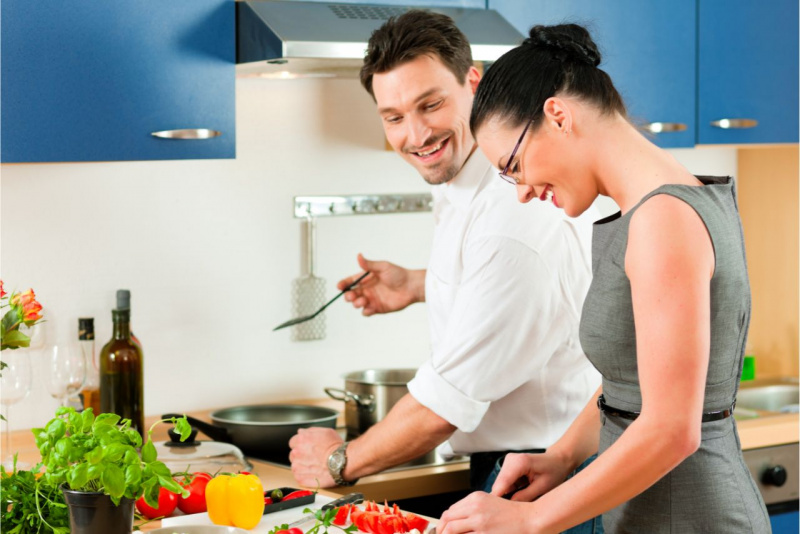 uomo attraente sorride alla donna mentre preparano da mangiare in cucina