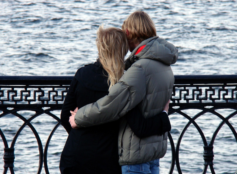 coppia uomo donna capelli biondi di spalle, abbracciati guardano il mare