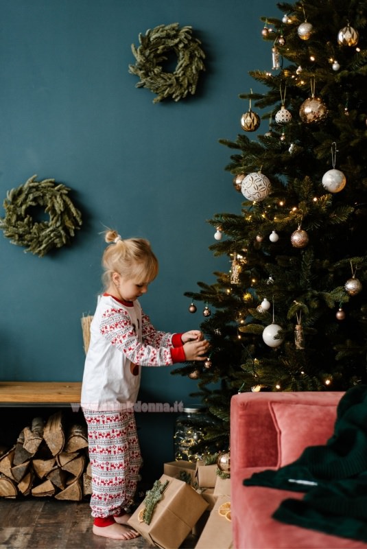 bambina decora albero di natale palline decorazioni natalizi regali legno divano velluto rosa luci 