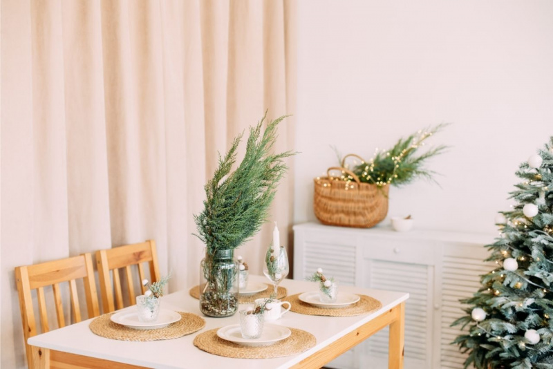tavola apparecchiata a festa di Natale stile minimal tovagliette rotonde di paglia tavolo sedie legno cesta rami abete verdi fresche albero 