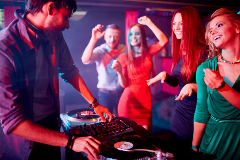 serata in discoteca bella donna capelli biondi vestito verde abito rosso guardano deejay mentre ballano