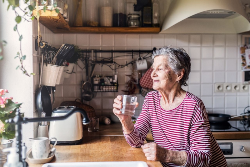 donna anziana beve bicchiere acqua davanti finestra cucina ondata di calore