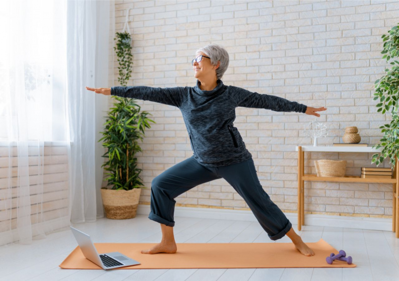 donna capelli grigi sorriso posizione yoga su tappetp casa