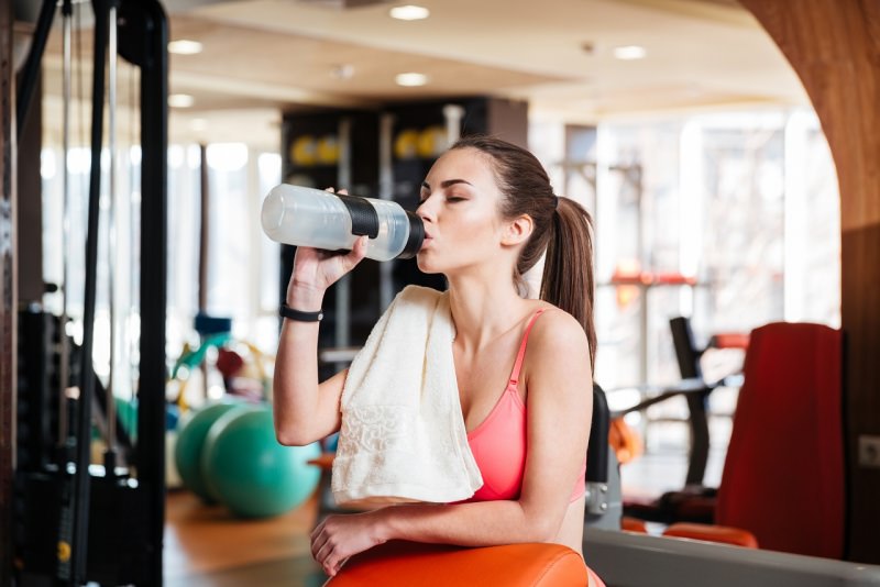 donna atletica si idrata in palestra beve integratore