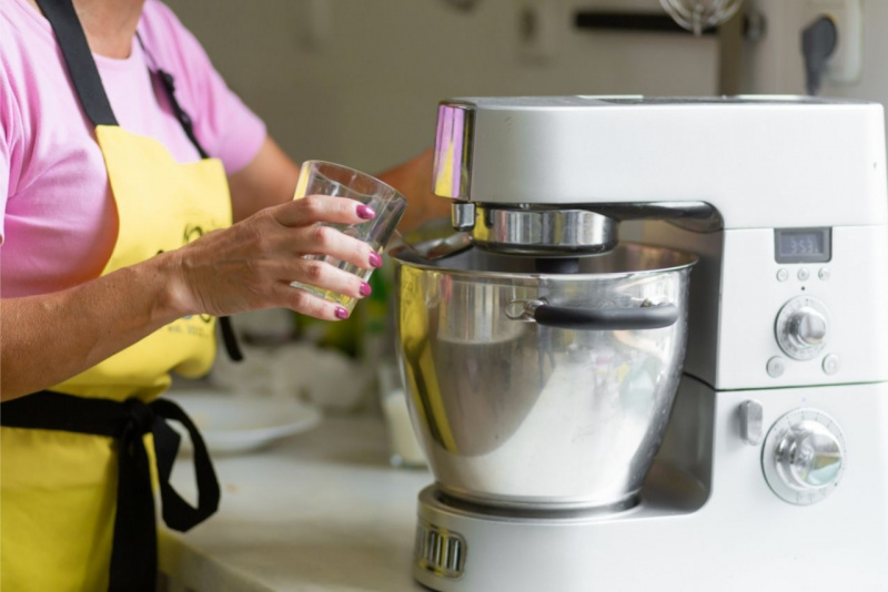 donna in cucina versa liquido nella planetaria robot grembiule