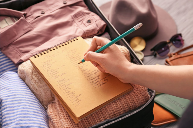 block notes su vestiti dentro valigia matita mano donna preparativi viaggio