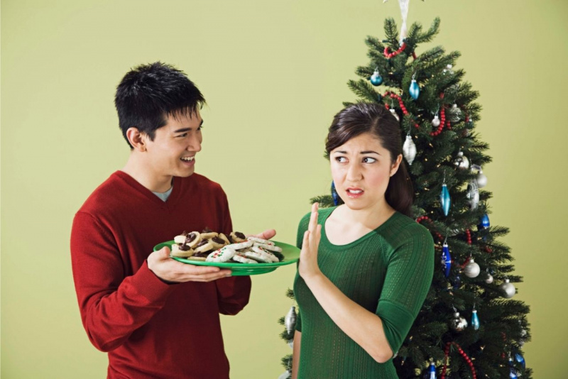 uomo offre biscotti natalizi su vassoio ma la donna li rifiuta davanti albero di natale