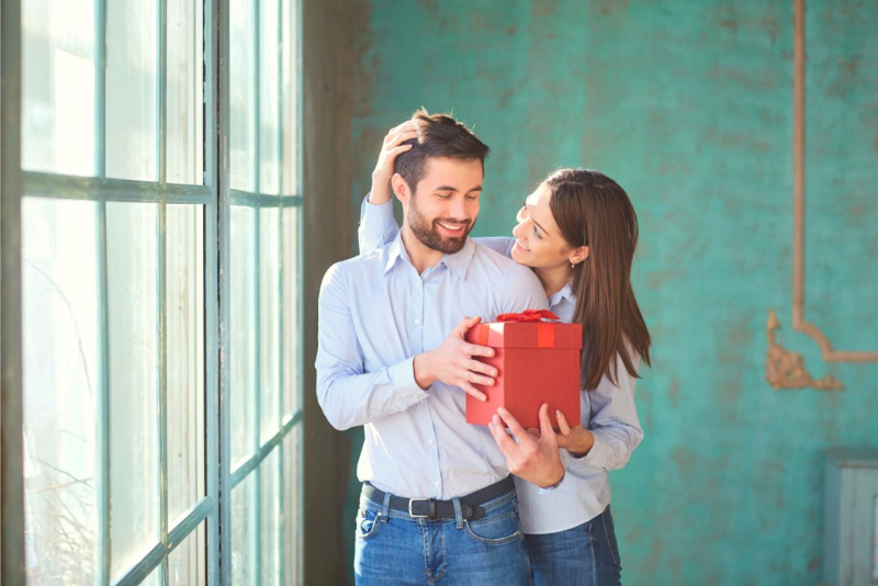 coppia bella donna accarezza uomo con barba mentre gli da pacco regalo 