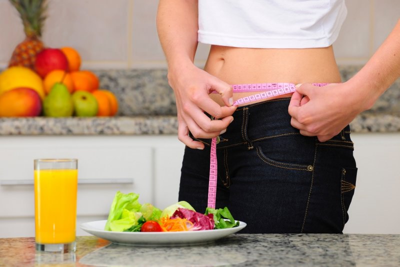 donna misura girovita con metro sarta piatto verdure insalata bicchiere arancia frutta