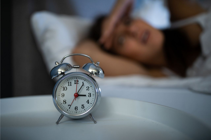 problemi di sonno donna sdraiata a leto con sveglia tre del mattino