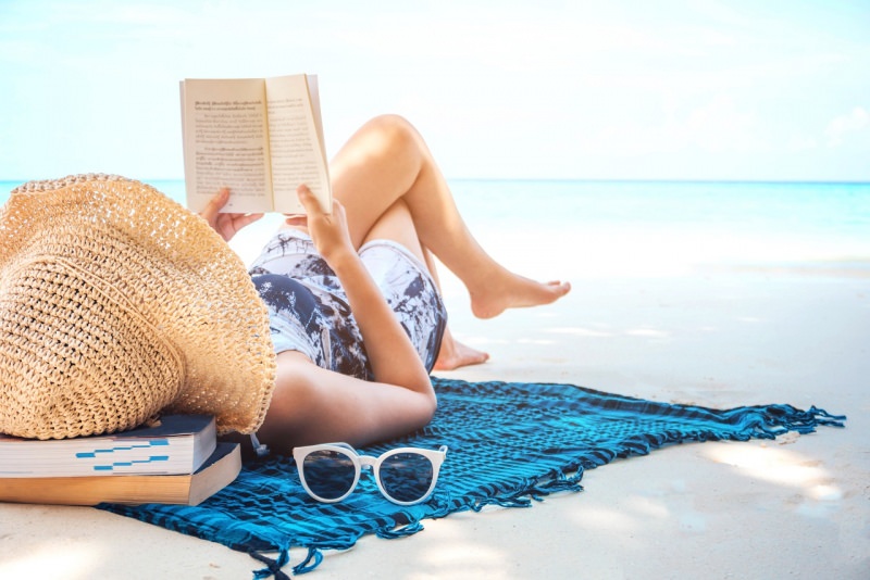 donna legge libro romanzo in relax sulla spiaggia mare estate cappello occhiali da sole
