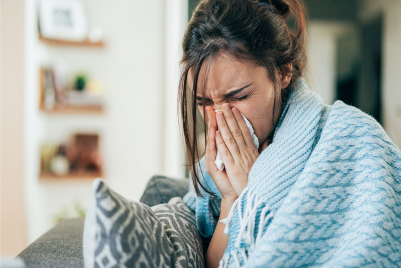 influenza raffreddore donna si soffia il naso fazzoletto cuscino divano plaid scialle azzurro