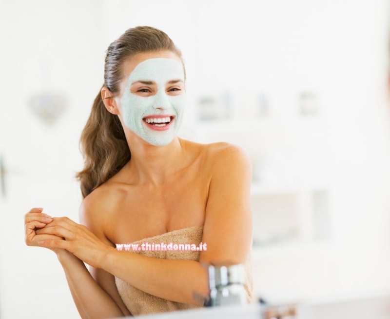 donna sorridente si guarda specchio bagno maschera di bellezza sul viso telo spugna