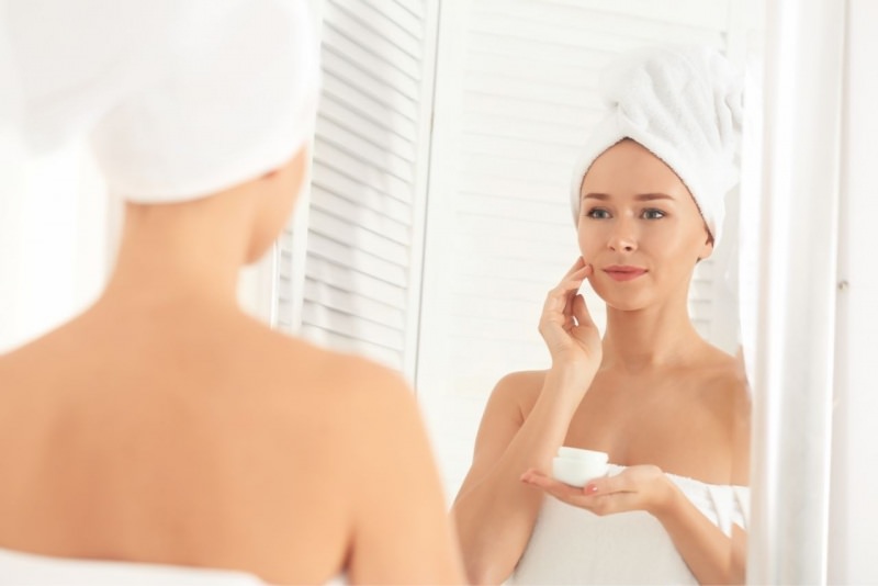 donna applica crema viso guardando specchio bagno telo spugna turbante