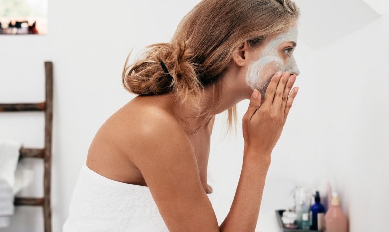 viso donna allo specchio bagno mette maschera di bellezza sul viso