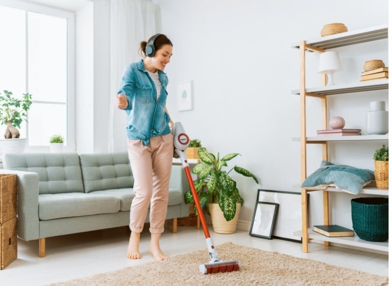 donna snella passa aspirapolvere mentre ascolta musica cuffie wireless pulizie casa soggiorno divano tappeto