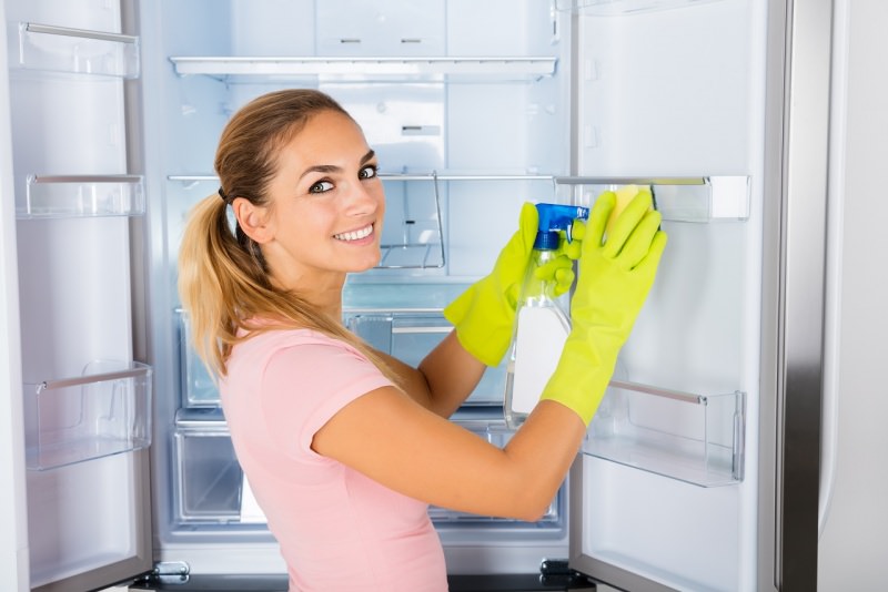 bella donna sorridente pulisce frigo vuoto con guanti e spruzzino