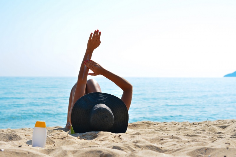 donna sdraiata sulla sabbia mare sole si spalma protezione solare cappello estate